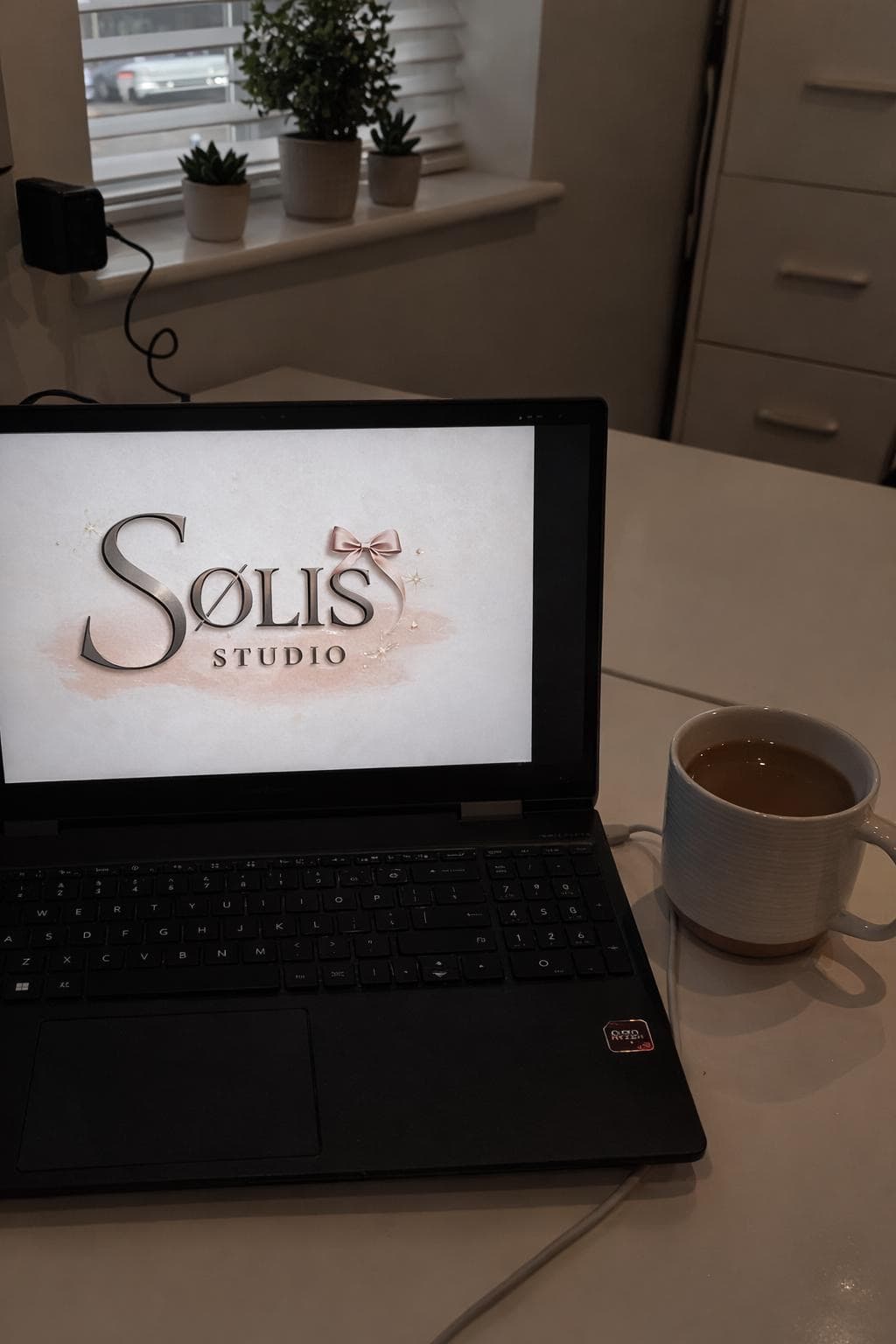 Alyssia's laptop on a desk, the SØLIS Studio mark on screen — where the brand was first drafted.