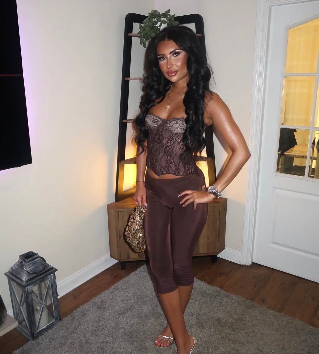 Alyssia in a brown lace corset and brown leggings, lit by a soft pink lamp.